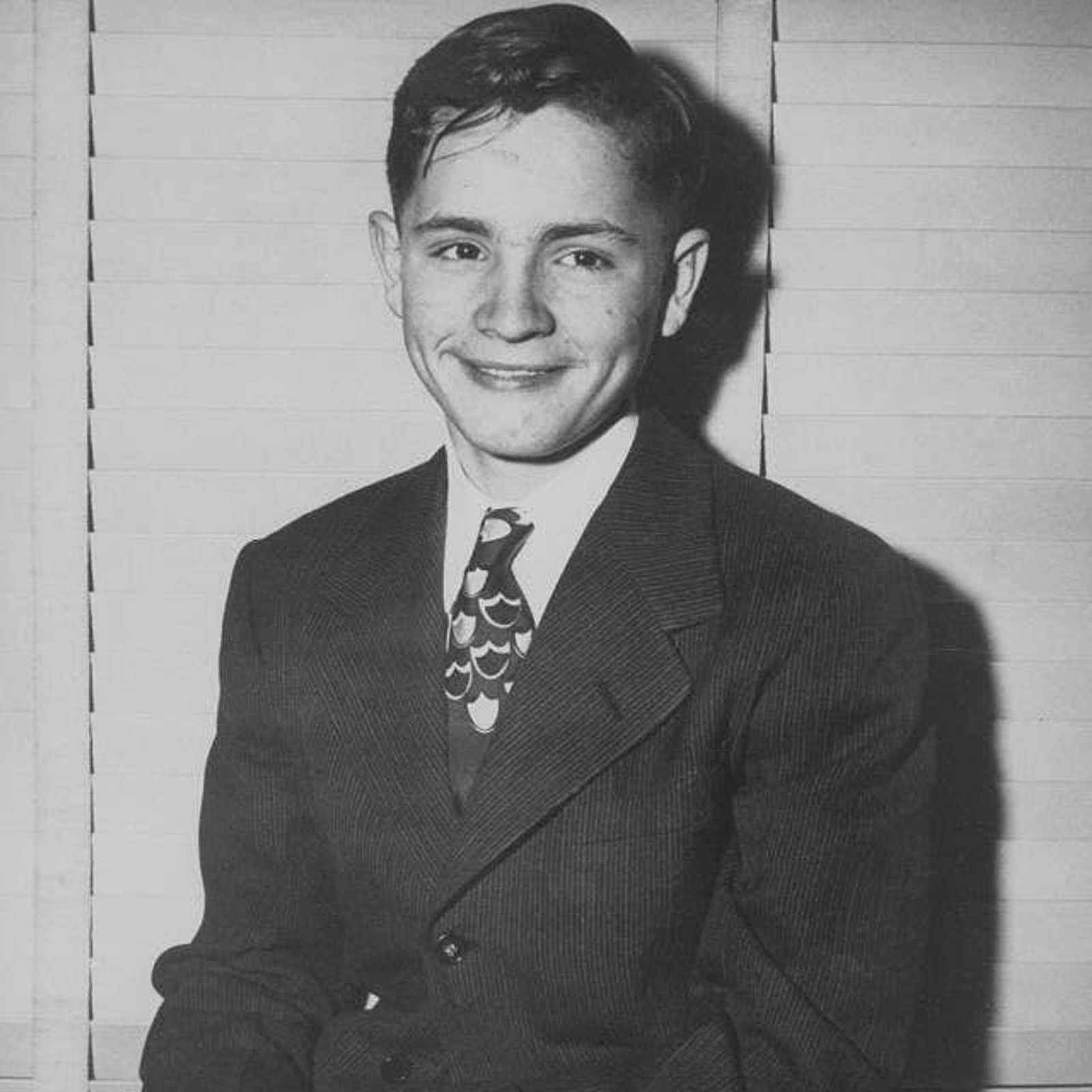 A young Charles Manson wearing a suit smiling, Photo Credit: DQD/X