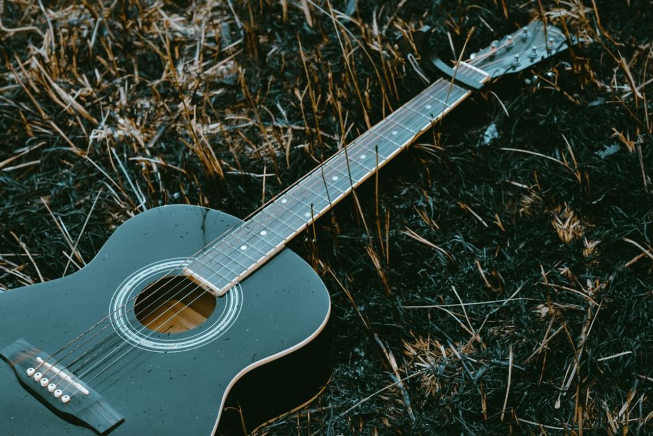 Close-up of an acoustic guitar placed on dry grass, capturing a serene, rustic vibe.