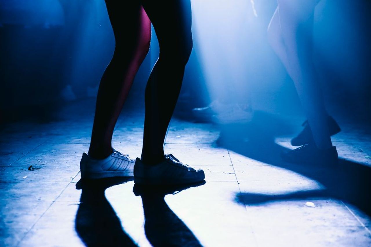 Vibrant silhouettes of people dancing on nightclub floor with dramatic blue lighting.