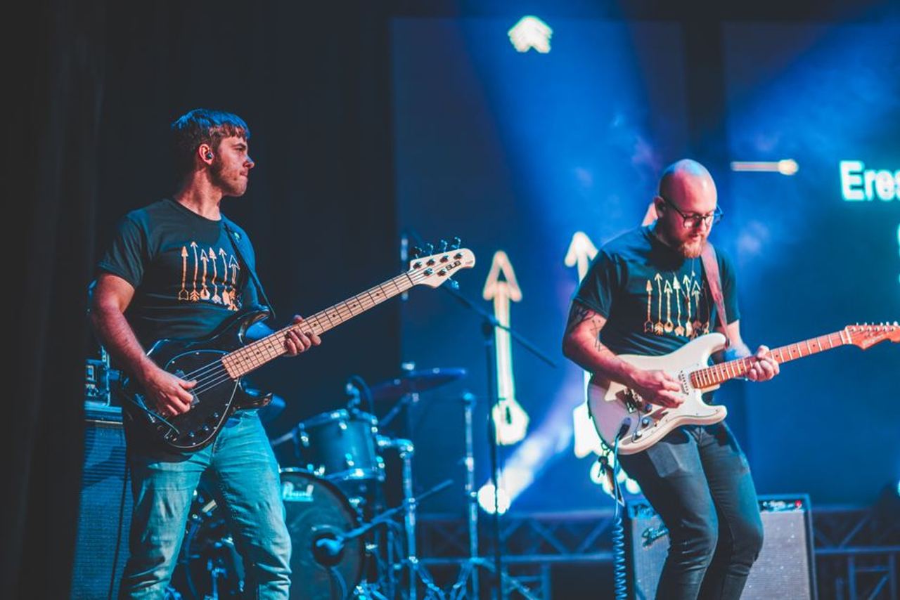 Energetic live performance featuring guitarists on stage with vibrant lighting.