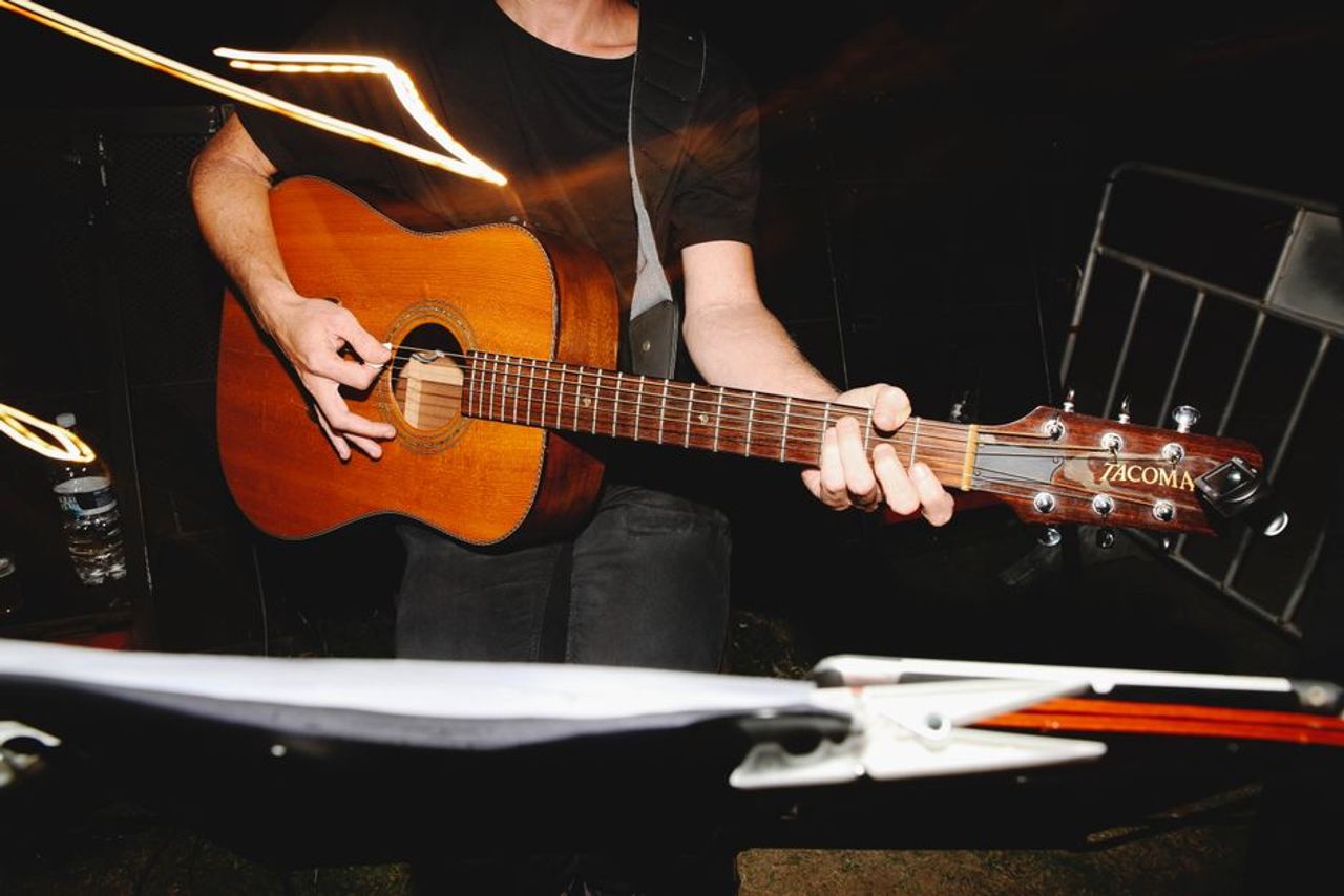 Musician strumming an acoustic Tacoma guitar outdoors at night.