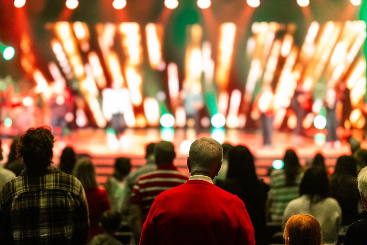 A diverse crowd watches a colorful stage performance in a lively concert atmosphere.