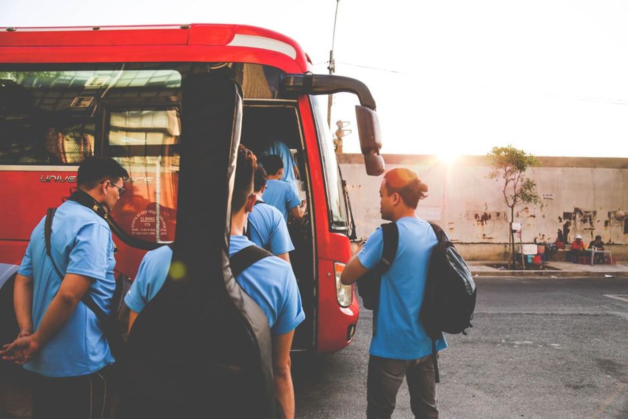 Musicians boarding a red bus in Tân Bình, Hồ Chí Minh City during sunrise. A lively street scene.